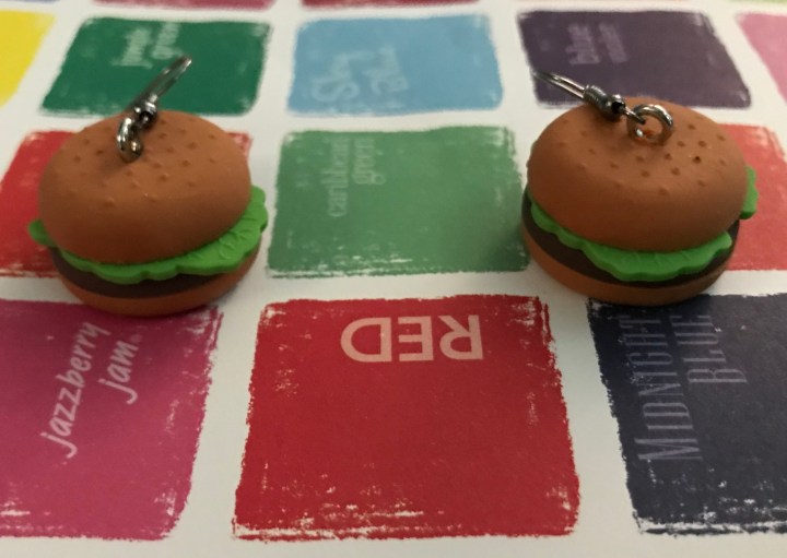 Image of miniature hamburgers as earrings on multicolored background.