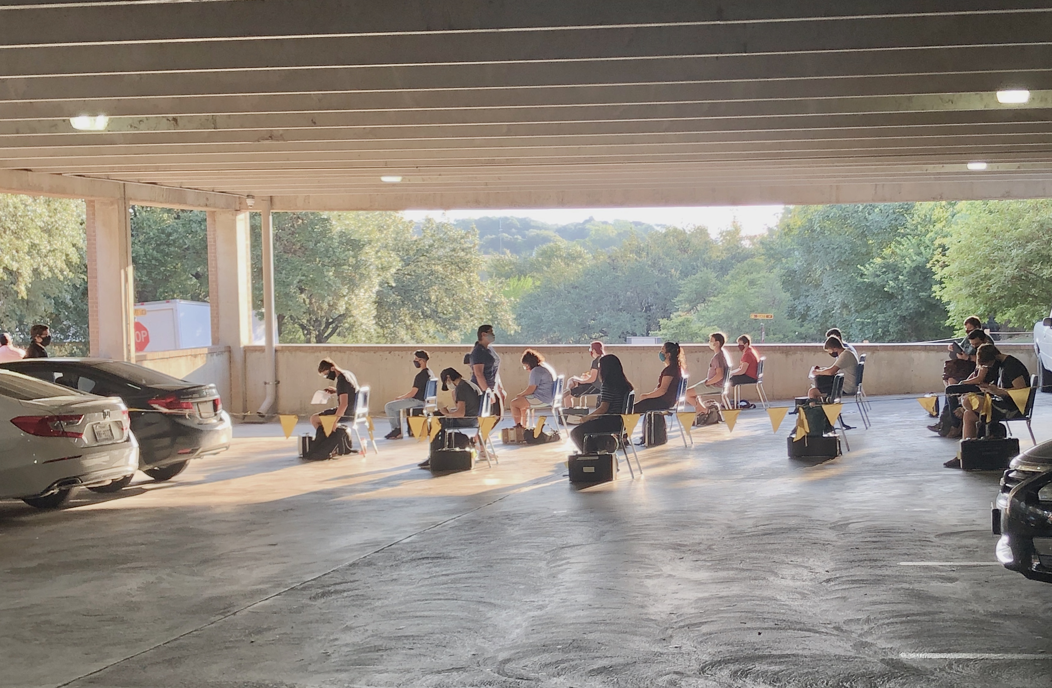 A photograph of students of a School of Music course participating in classwork in a reserved area of the Pleasant Street parking garage. Featured in the image are various students seated in classroom chairs and with instruments by their sides.