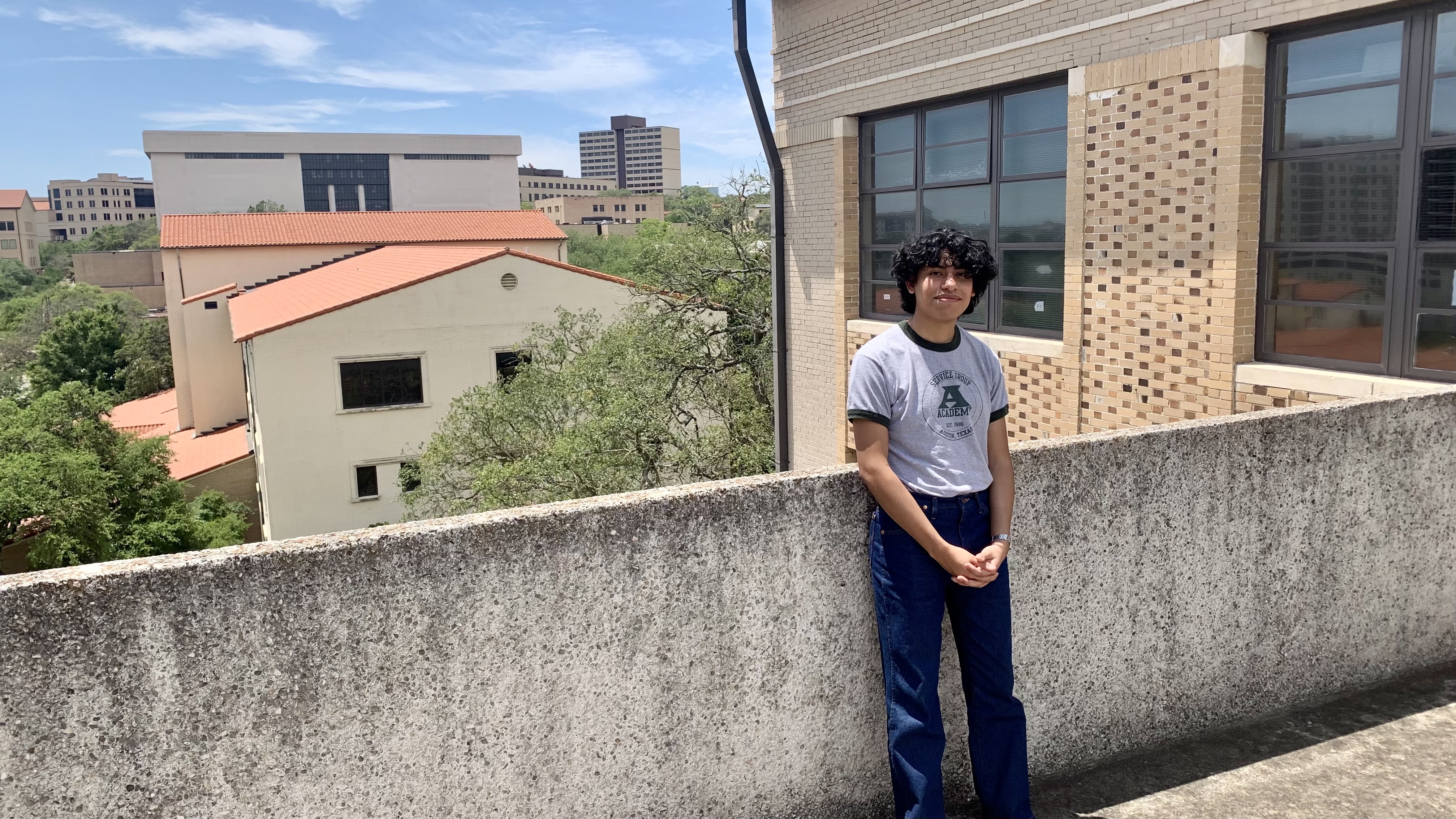 Jesse Rodriguez is posing with his finger tied on balcony overlooking the Texas State campus.