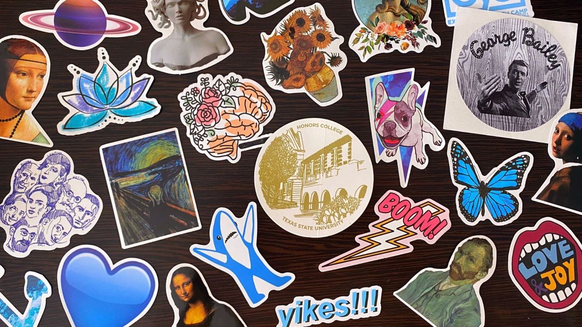 Photo of various stickers organized in a collage on a table. Stickers include from left to right The Lady With an Ermine by Da Vinci, illustrated portraits of classic artists, a purple planet resembling Saturn, a blue heart Apple emoji, a line drawing of a lotus flower, The Scream by Munch, a marble bust of Medusa, Mona Lisa by Da Vinci, an illustrated human brain with roses, a Super Bowl shark, a golden illustration of the Texas State Honors College, Arles Sunflowers by Van Gogh, blue text reading “yikes” with three exclamation points, a lightning bold with text reading “boom”, a white bulldog with a painted pink lightning bolt on its face in front of a blue lightning bolt, a circle portrait of The Birth of Venus by Botticelli with roses underneath, Self Portrait by Van Gogh, a Blue Morpho Butterfly, a greyscale circle sticker reading “George Bailey” with character from It’s a Wonderful Life, open mouth with red lips inside reading “love and joy” and Girl with a Pearl Earring by Vermeer.