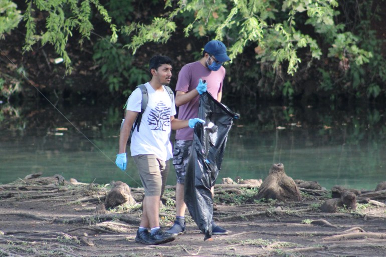 Two students looking for litter near Purgatory Creek in Rio Vista Park. They are each holding a trash bag in one hand. 