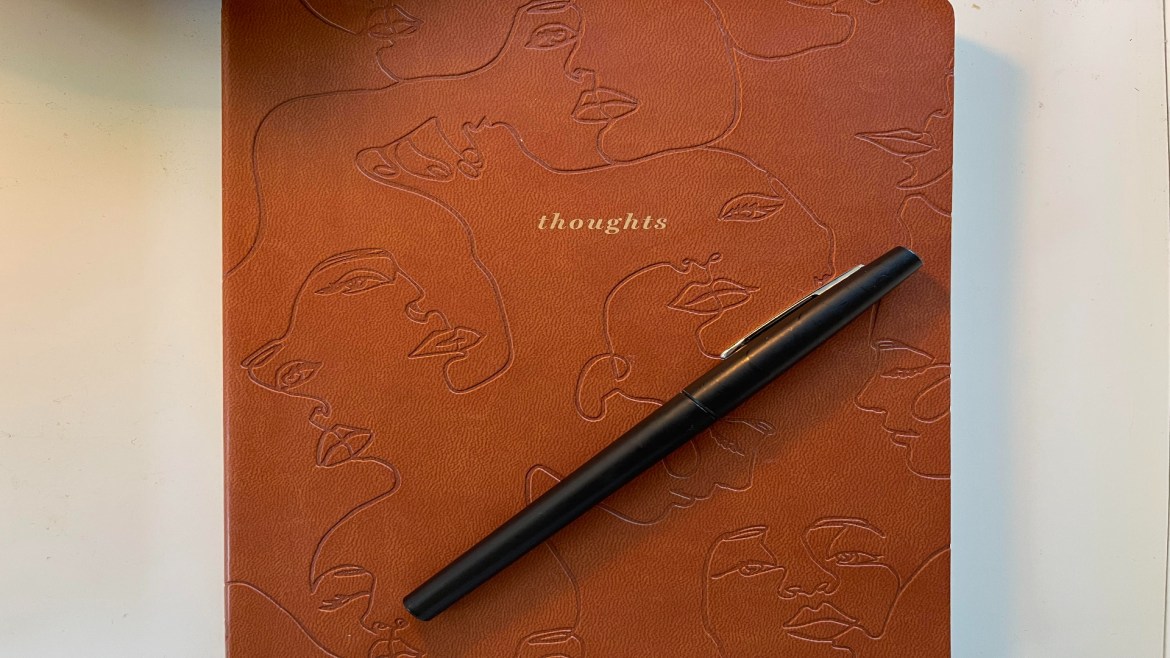 A brown journal labeled thoughts with faces engraved into the notebook lying on the desk.