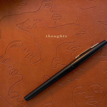 A brown journal labeled thoughts with faces engraved into the notebook lying on the desk.