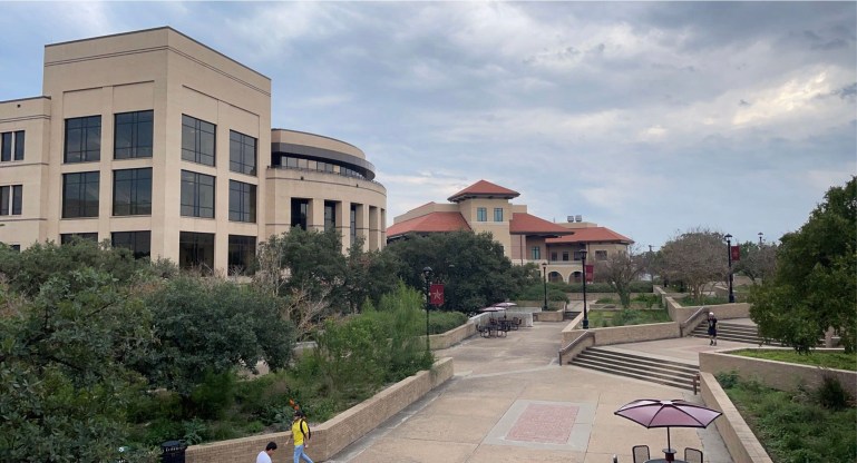 Shot of campus from LBJ Student Center overlooking the McCoy College of Business Administration and Ingram School of Engineering with a couple of students passing through empty pathways.