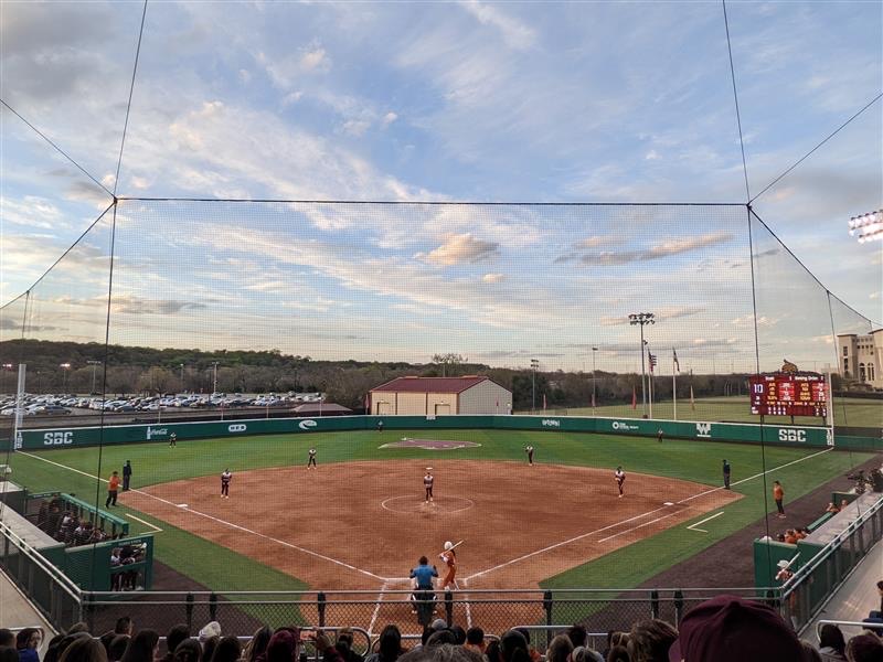 View of the Bobcat softball stadium from the top of the stands behind the batter’s box. Texas State stands in defensive positions waiting for Jessica Mullins to pitch the ball. Texas has a batter in the box waiting for the pitch.