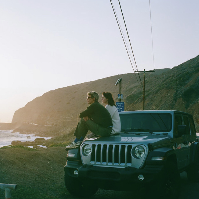 Single Cover Art features a man and woman sitting on the hood of a Jeep Wrangler, overlooking a rocky coastline as the sun sets.