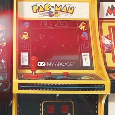 Three mini classic arcade games side by side. On the far left, a black game with red buttons and colored stickers with “Galaga” written on the top. In the middle, a yellow game with red buttons and “Pac-Man” written on the top. On the right, a yellow and white game with red buttons with a multi-color “Mappy”written on the top. There is a red and white hue overlay on the photo.