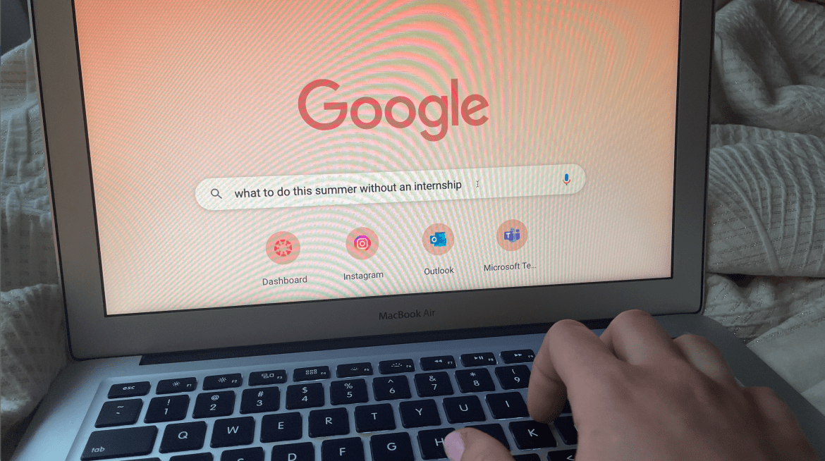 A laptop screen on the google search page. The search bar says “what to do this summer without an internship” and the fingers of the person searching it are on the keyboard towards the bottom right corner of the picture.