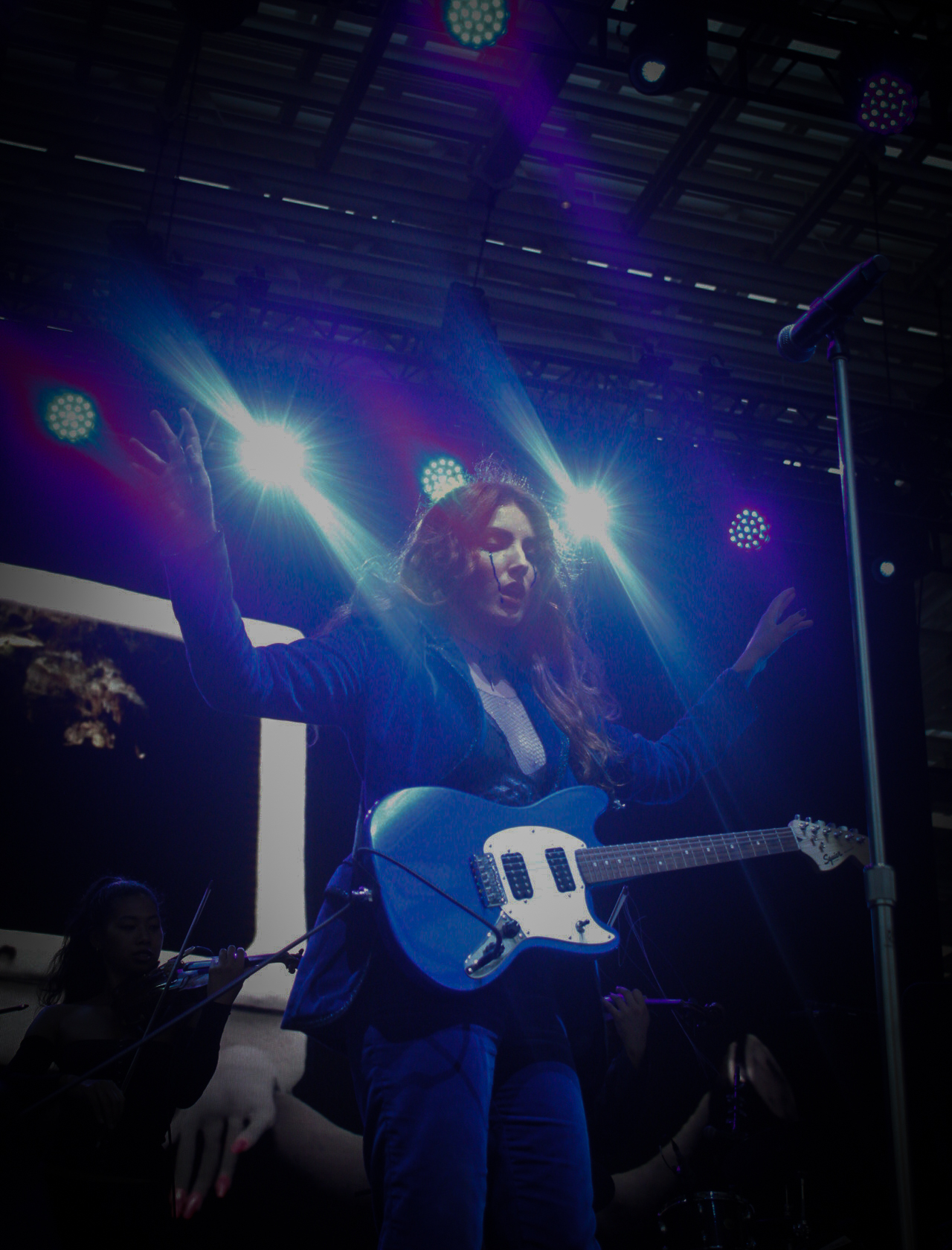 Haley Dahl with a blue electric guitar, illuminated by blue stage lights. 