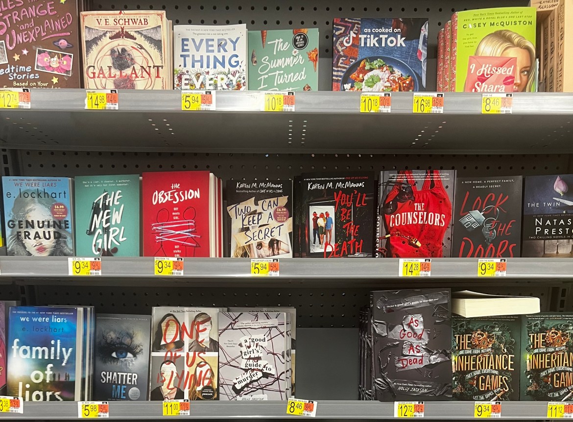 A large selection of young adult books sit in a Walmart book aisle.