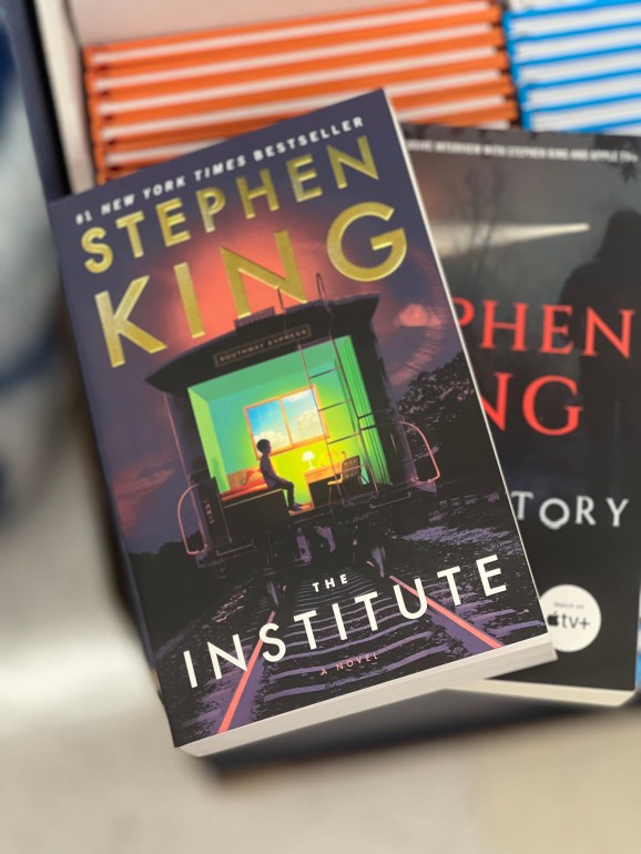 Stephen King’s “The Institute” is layered on top of another book that I purchased in a small book shop.