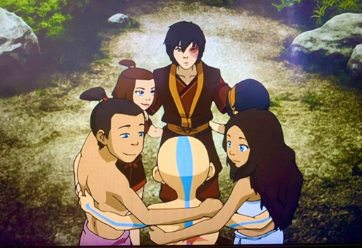 The main characters of Avatar: The Last Airbender are shown exchanging a group hug, smiling and looking at each other fondly.