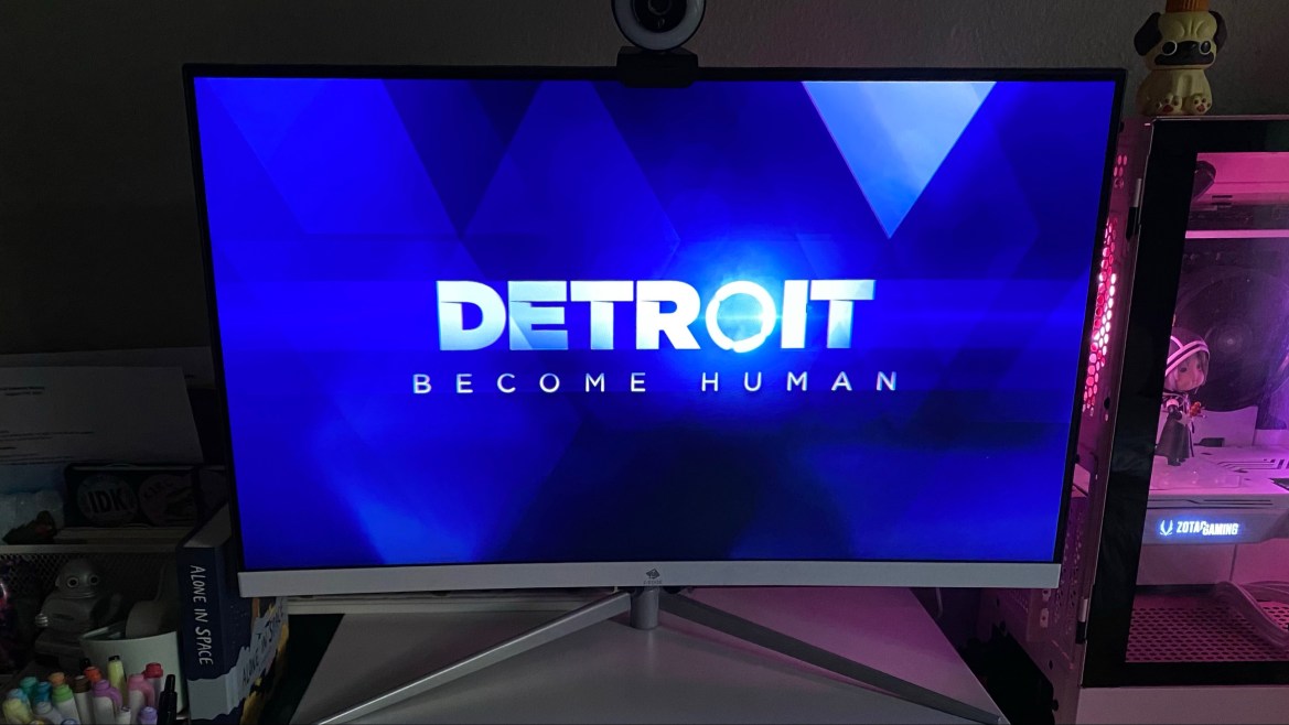 Bold, white, all-caps center text, reads “DETROIT”. The “O” in “Detroit” is a glowing LED. The LED represents the external feedback component, attached to the temple of each android. Beneath“DETROIT”, the subtitle reads “BECOME HUMAN” in a small white, all-cap, font. The background is a series of overlapping rhombi, in various shades of blue.