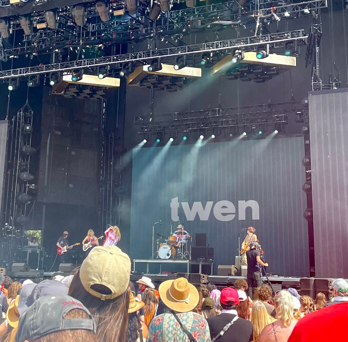 Twen at Austin City Limits 2022 ALT-TEXT: The image features the members of Twen performing onstage. The screen behind them is black with the name twen in gray. The backs of various people’s heads are seen in the forefront.
