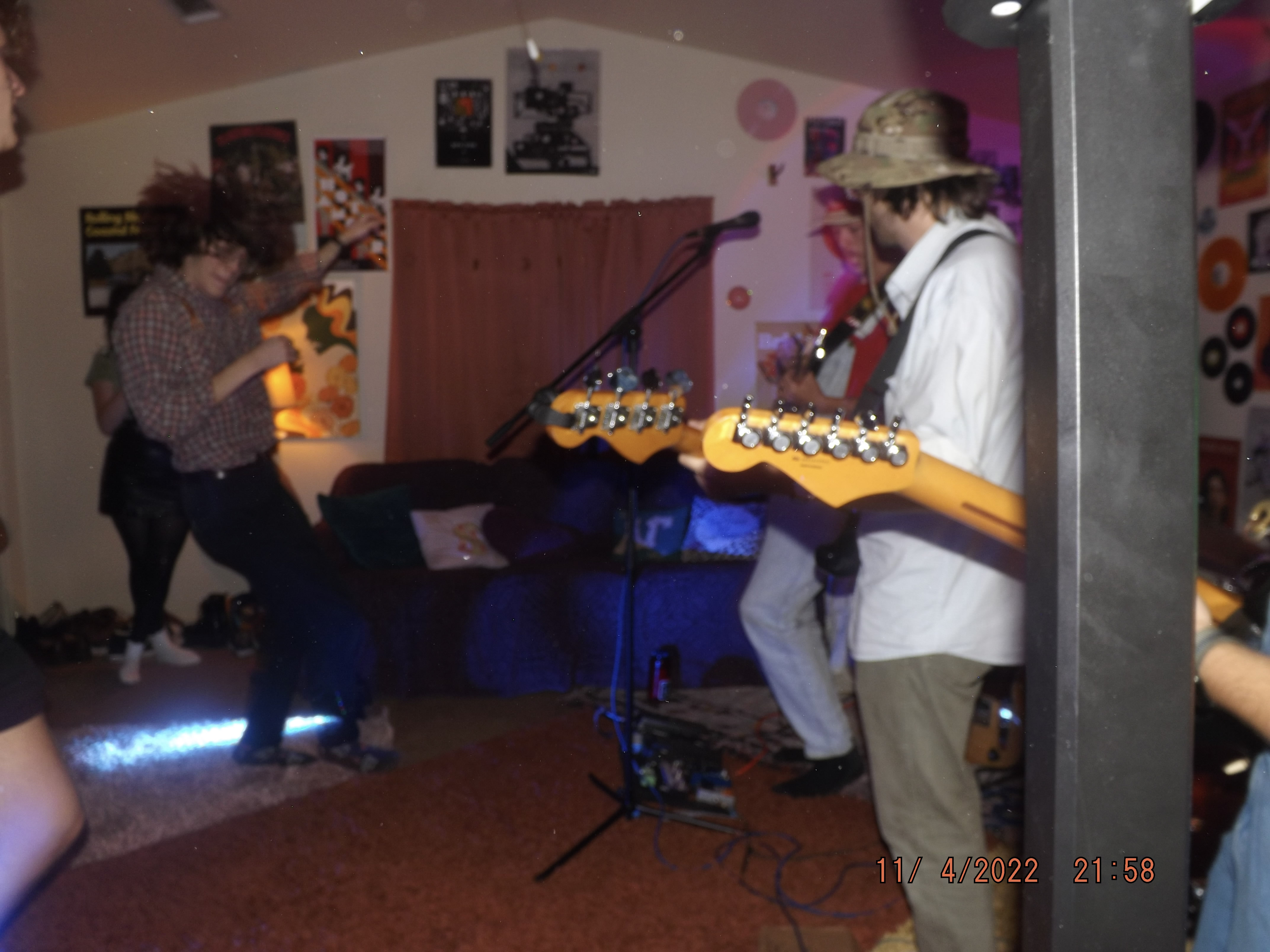  Image features a hazy depiction of Curtis Rowe and Ethan Lugbauer (out of frame) moshing in the living room of Earle’s Basement during Say So’s set. Say So’s West, Cicero, and Russell are opposite Rowe. “11/4/2022 21:58” can be read in the bottom right corner of the image.