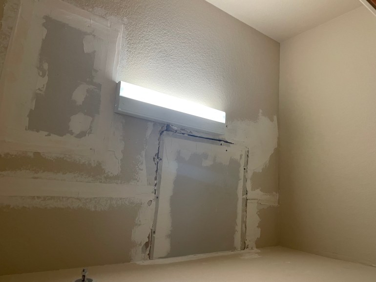 The photo is of a ceiling with two large patched squares. There is a vertical light in the center of the ceiling.