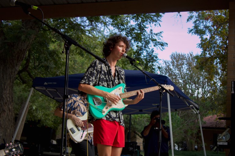 Garrett Douglas (center) plays teal electric guitar and sings into a mic.  