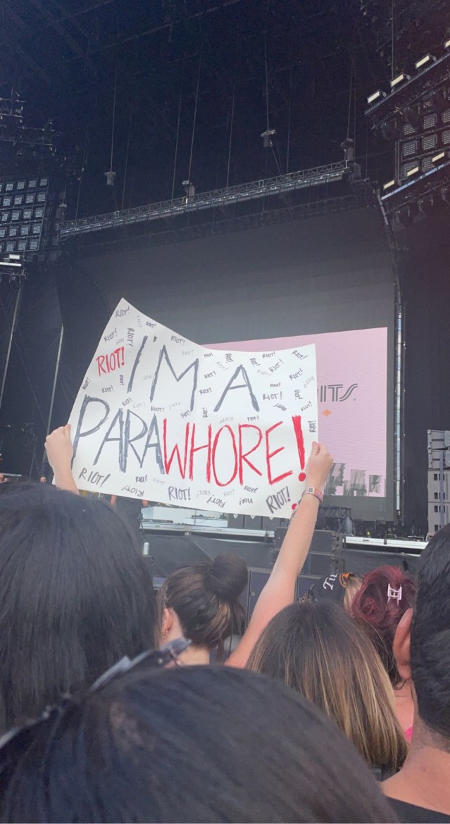 A fan at the barricade holding up a sign that reads “I’m a ParaWhore” in the font and style of Paramore’s Riot album cover art.