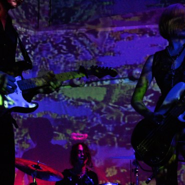 Kivlen (left), Faber (drums), and Cummings (bass) underneath purple lights.