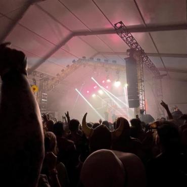 a wide-angle photo taken from the crowd of a concert with bright lights and hands in the air.