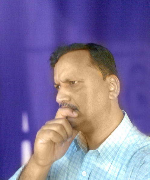 A man, who is not the author, is pictured from the chest up and facing to the left. He has his finger up to his chin in an obvious gesture of intent thinking. He is wearing a blue plaid shirt, has a mustache, and is set against a purple background.