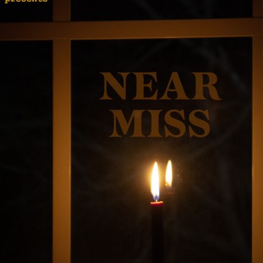 Black candle in front of a window. Near Miss is above it