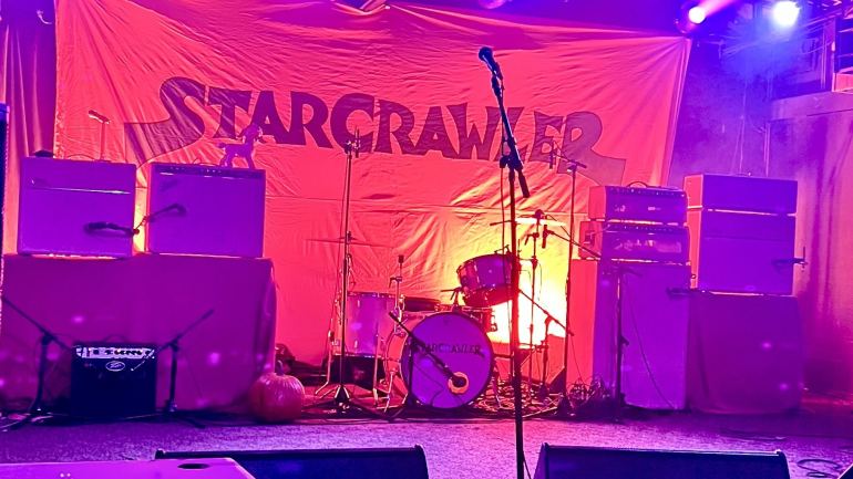 A stage with various guitar amplifiers, cables, and drums all painted to the same matching shade of pink