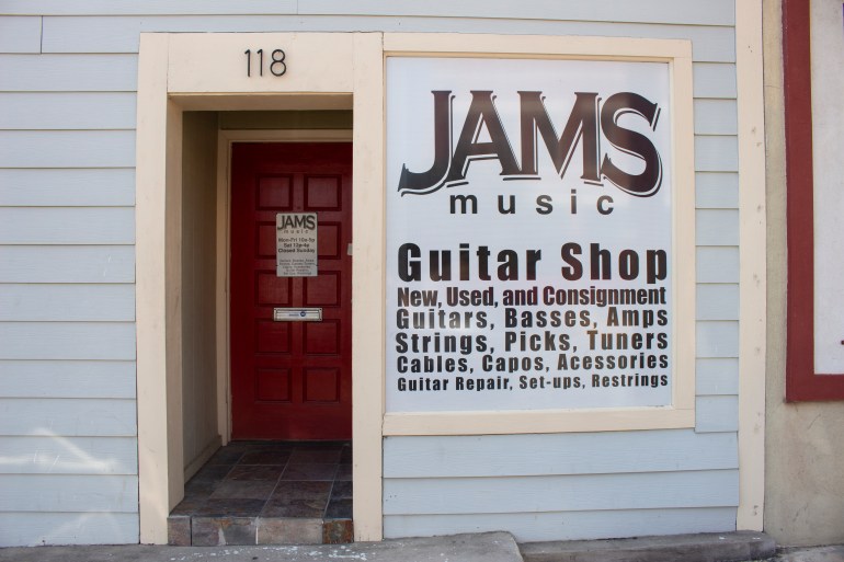 Front of the JAMS music store. A red door with a sign and the window with the word JAMS written across. 