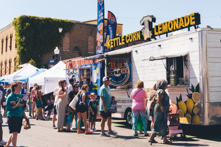 Festival Goers stand in line for fresh kettle corn and lemonade as others walk past.