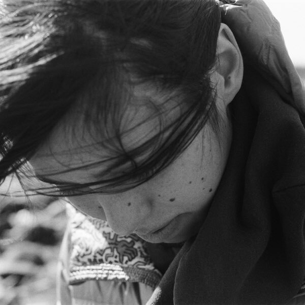 A black and white photo of a woman with her hair blowing across her downturned face