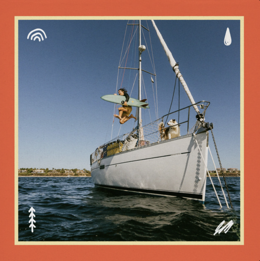 This image shows Goth Babe jumping off his sailboat into the ocean with a surfboard while his dog watches from on deck.