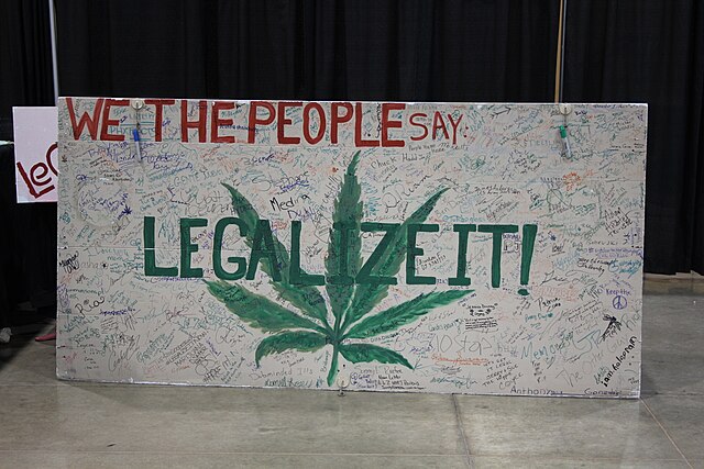 sign saying "We the people say" "Legalize it!" with marijuana leaf in background.