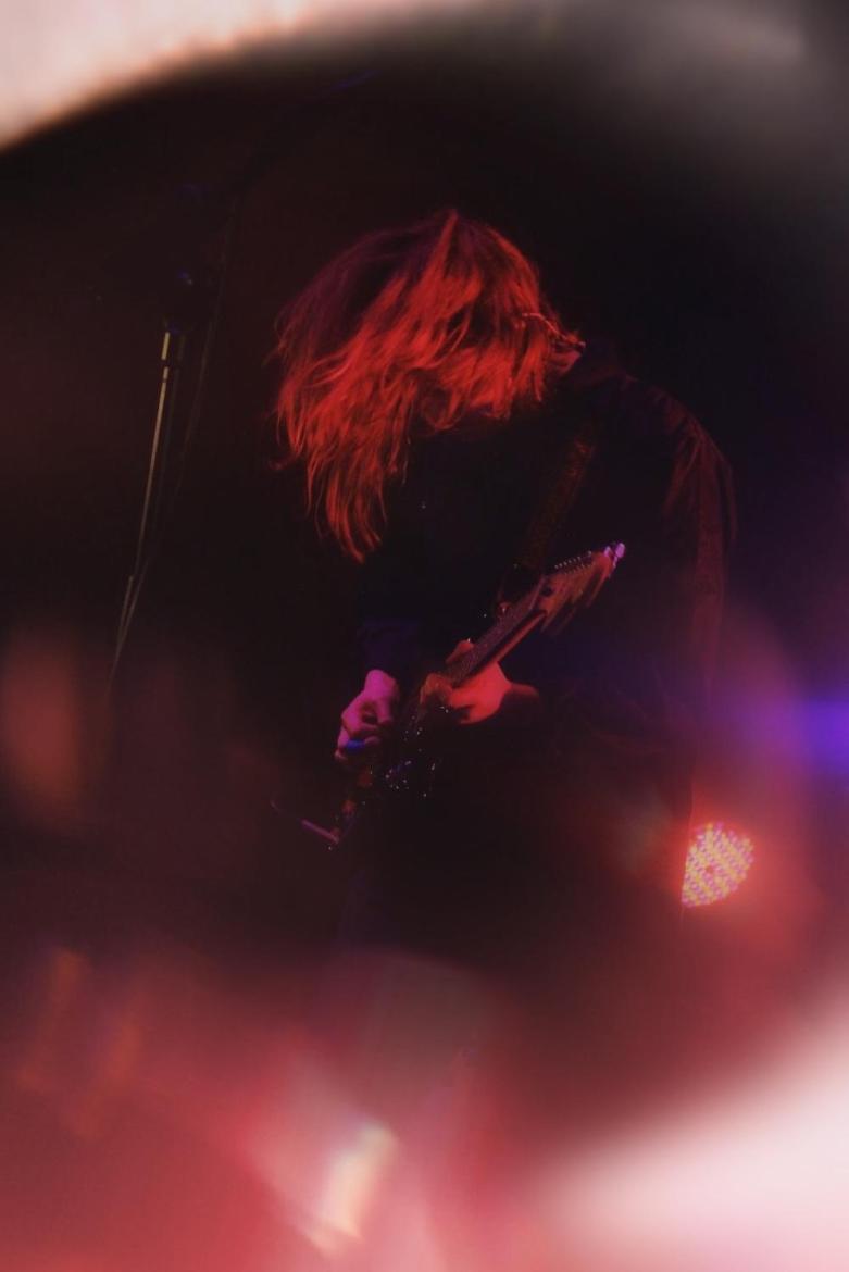 Marika Hackman playing guitar with red and purple lights shining on her.