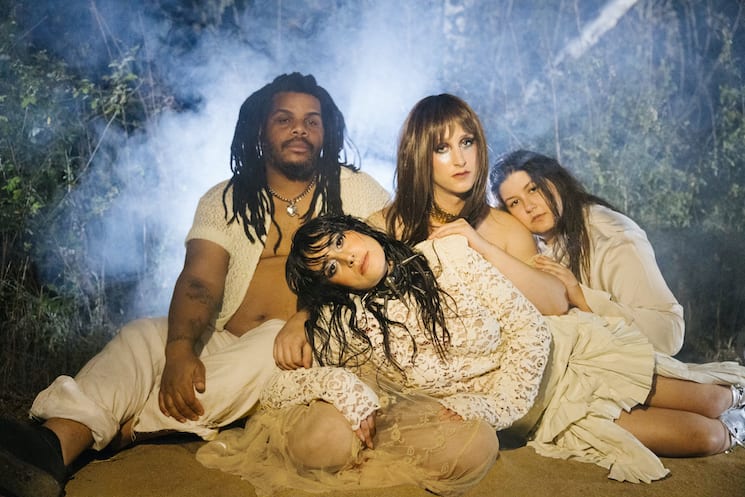 Mannequin Pussy band in a photoshoot behind a grey dark blue background all members dressed in white. 