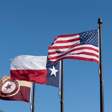 Blue sky background with the American, Texan and Texas State flag blowing in the air.