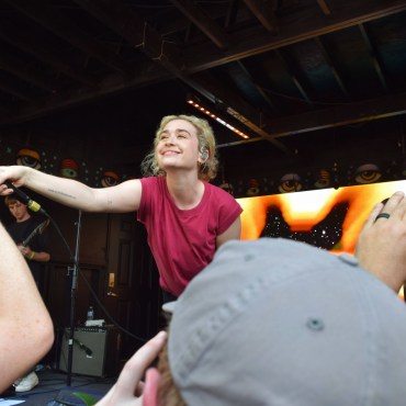 Blondshell in pink shirt on stage pointing microphone to crowd.