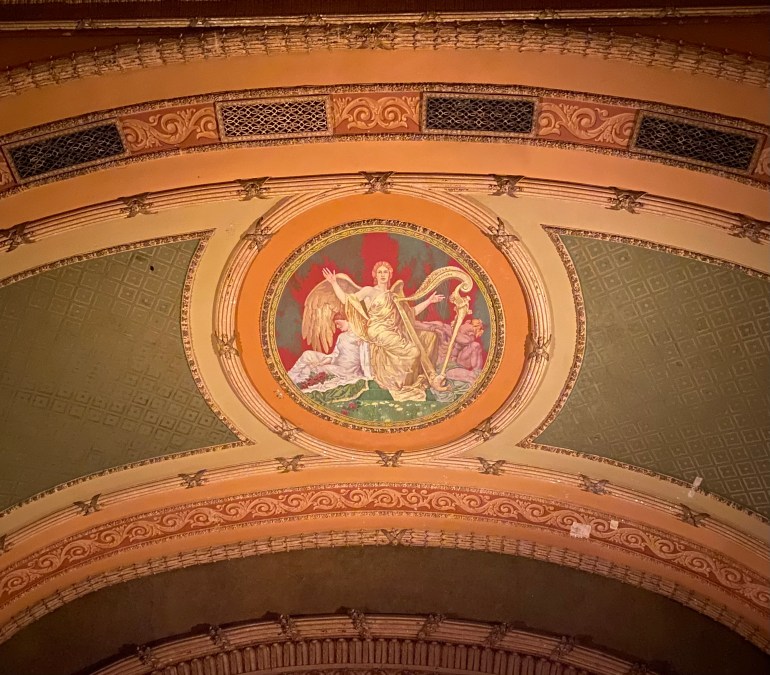Old painting on ceiling of female angel holding a harp with two angel figures behind her