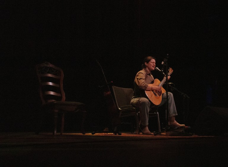 Artist Adrianne Lenker sing on a dark stage with a guitar