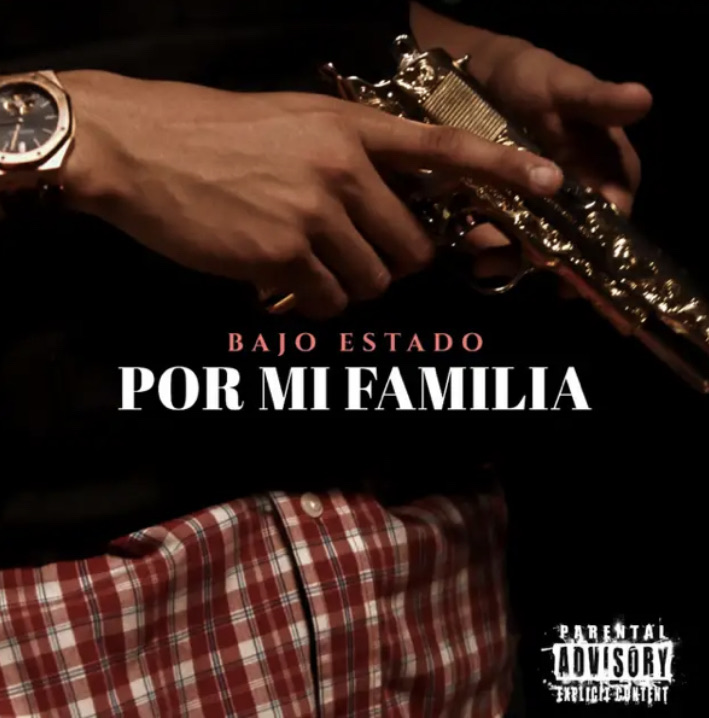 A person wearing checkered pants and a black shirt holds a pistol, wearing a watch. In the middle “Por Mi Familia – Bajo Estado” is written. 