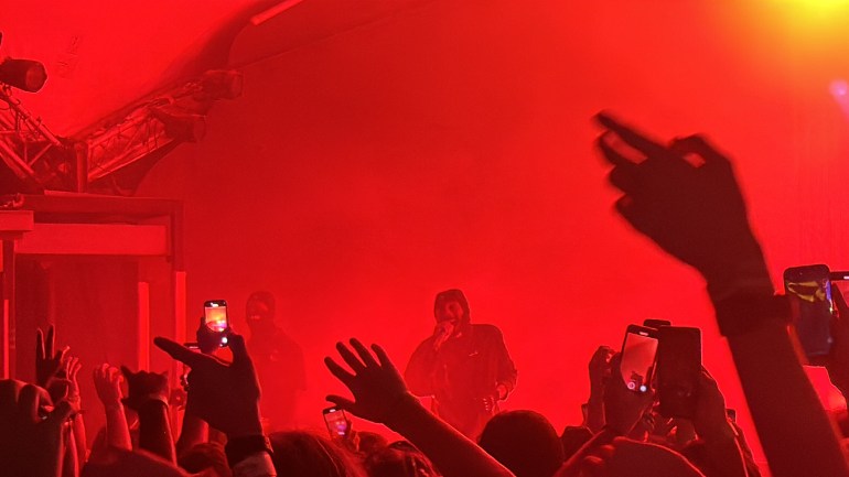 JPEGMAFIA performs “vulgar display of power” under red stage lights, creating a fiery ambiance as fans reach out toward the stage.