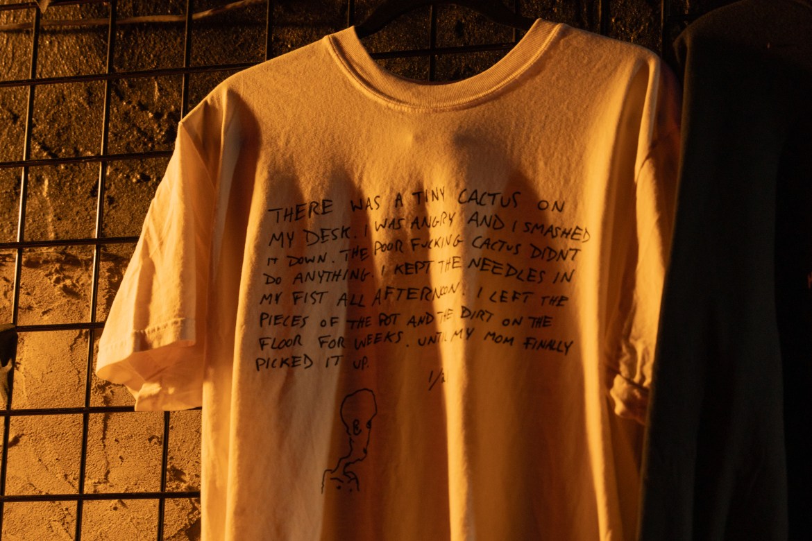 he T-shirt features the cover of Horse Jumper of Love’s self-titled album. The words on the album cover read, “THERE WAS A TINY CACTUS ON MY DESK. I WAS ANGRY AND I SMASHED IT DOWN. THE POOR FUCKING CACTUS DIDN’T DO ANYTHING. I KEPT THE NEEDLES IN MY FIST ALL AFTERNOON. I LEFT THE PIECES OF THE POT AND THE DIRT ON THE FLOOR FOR WEEKS. UNTIL MY MOM FINALLY PICKED IT UP. 1/21”. There is also a drawing of the back of a person’s head underneath the text to the left.