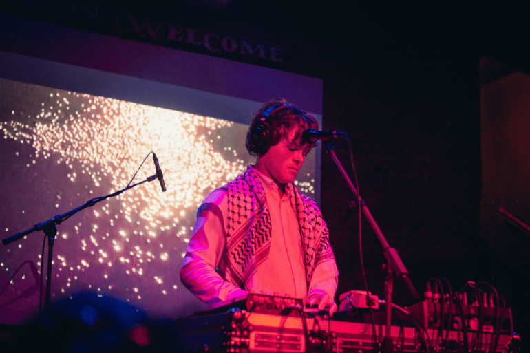 Warren Hildebrand (Foxes In Fiction) playing the keyboard on stage. The lights have a pink and purple hue. 