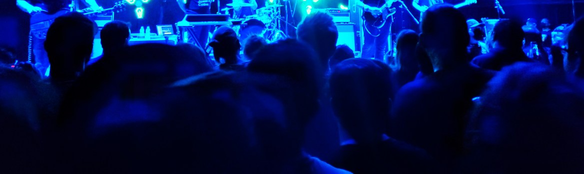 Small concert crowd close to stage under dark blue lighting. 