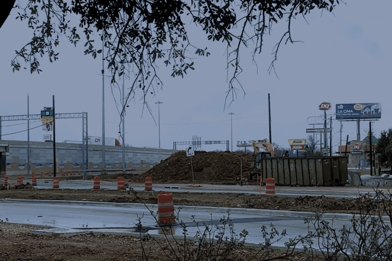 Construction on an empty street, with traffic cones and a dirt pile off to the side of the road on a rainy day.