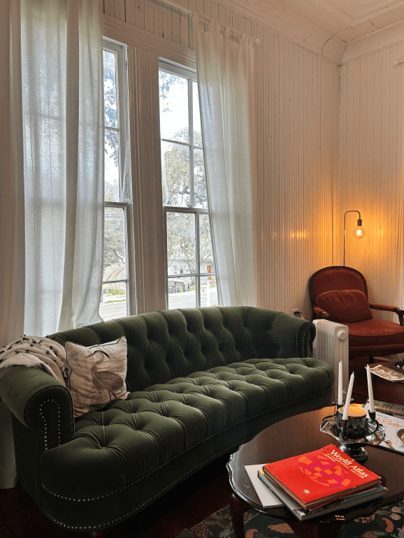 Green couch in front of a window in the sitting area inside the Green Heron Bookshop.