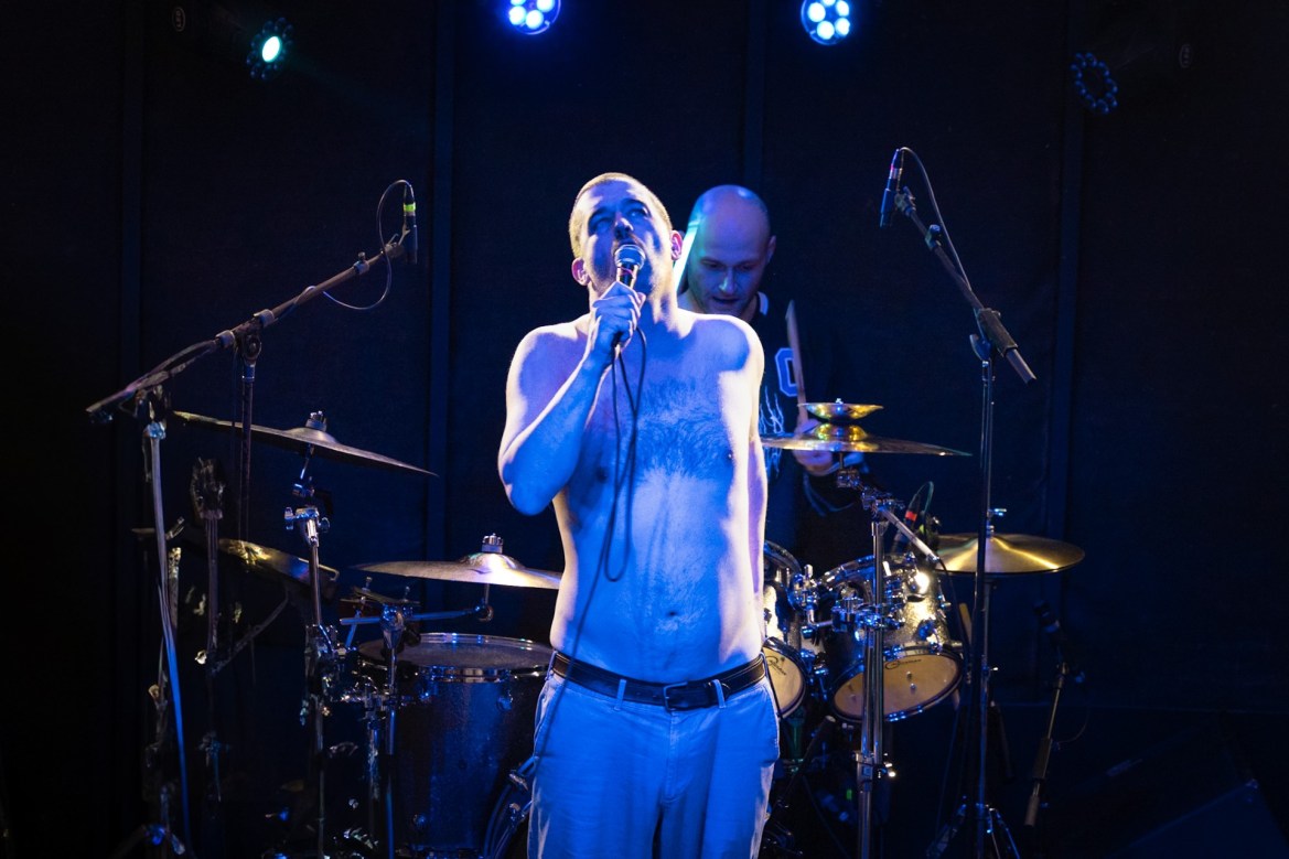 Photo of Raygun Busch of Chat Pile on stage at Mohawk Austin. A cascade of blue lighting washes over him as he screams into the mic.