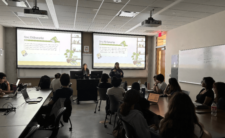 Members of the Girls Who Code gather at a meeting and watch a powerpoint being presented in the classroom by the officers. The Powerpoint slide shown talks about their philosophy. 