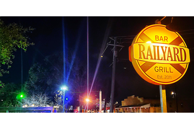 Roadside night photo with a lit-up sign for The Railyard bar and grill in the right-hand corner. 