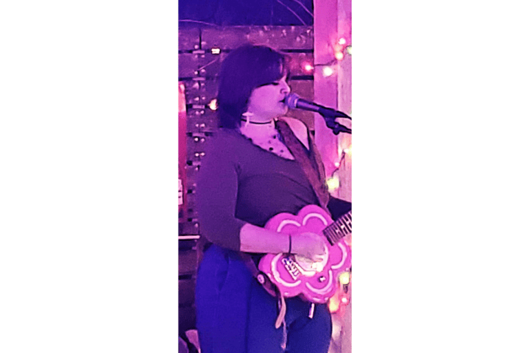 Lead singer for keepsake mid performance playing a pink flower guitar in night lighting 