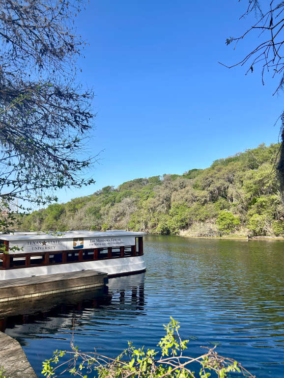 Glass-bottom boat floating on the Spring Lake water with green, tree-filled hill in the background.